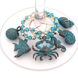 May include: Set of six turquoise and gold-toned wine glass charms featuring a crab, a seahorse, a fish, and three different seashells.