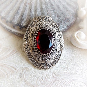 May include: A silver brooch with an ornate design and a large, dark red gemstone in the centre.