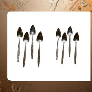 May include: A collection of silver serving spoons with textured handles and broad, leaf-shaped bowls. The spoons are arranged in two groups, each containing four spoons, against a white background.