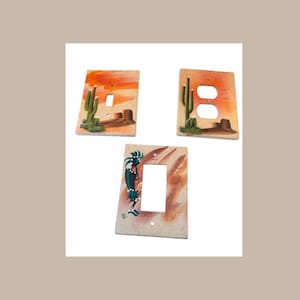 以下が含まれることがあります： 南西部の砂漠をテーマにした装飾的なライトスイッチカバー3つ。カバーには、サボテン、夕焼け、スタイリッシュな鳥が描かれた砂漠の風景が描かれています。