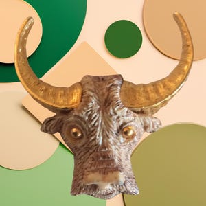 Puede incluir: Una escultura de cabeza de toro de color dorado y marrón con grandes cuernos. La escultura está colocada sobre un fondo de círculos verdes y beige.