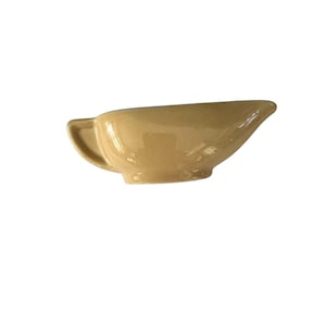 May include: A small, tan-colored ceramic gravy boat with a handle on one side and a spout on the other. The gravy boat has a glossy finish and a classic design, suitable for serving sauces and gravies.