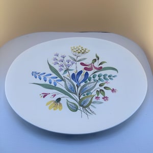 May include: A white ceramic plate with a floral design. The flowers are painted in shades of blue, yellow, pink, and green.