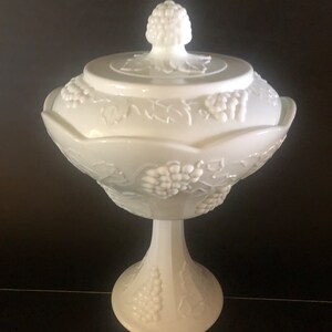 May include: White milk glass candy dish with a grape design and a lid. The dish has a pedestal base.
