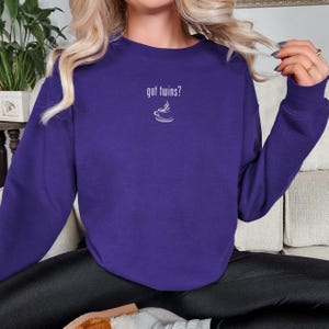 May include: A purple sweatshirt with the text "got twins?" above a small white coffee cup design. The long-sleeved top is made of a soft material and is suitable for casual wear. The sweatshirt is a solid color.
