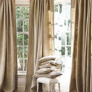 May include: A set of natural linen curtains with a rustic, farmhouse aesthetic. The curtains are hung on a window with a view of trees and greenery.