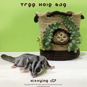 Könnte beinhalten: Eine gehäkelte braune und grüne Baumhöhlen-Tasche mit Kordelzug. Die Tasche ist für Zuckergleiter konzipiert und hat ein Blattdesign. Ein Zuckergleiter sitzt auf einer weißen Oberfläche vor der Tasche.