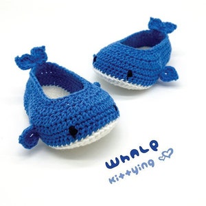 Puede incluir: Un par de zapatos de beb&eacute; de ballena tejidos a crochet en azul con detalles blancos. Los zapatos tienen un dise&ntilde;o simple con una cola y una aleta de ballena en cada zapato. El texto "WHALE Kit+Ying" est&aacute; escrito en la superficie blanca debajo de los zapatos.