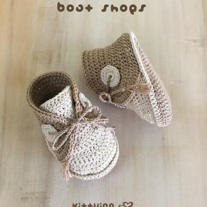 May include: A pair of crocheted baby booties in beige and white with a button detail. The booties are called "boot shops" and are made by Ki++ying.