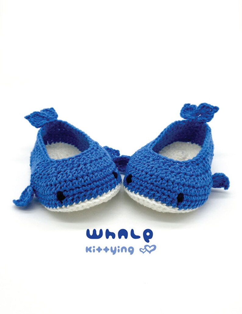 Puede incluir: Un par de zapatos de beb&eacute; de ballena tejidos a crochet en azul con detalles blancos. Los zapatos tienen ojos negros y una boca blanca. El texto "WHALE kit+ying" est&aacute; impreso debajo de los zapatos.