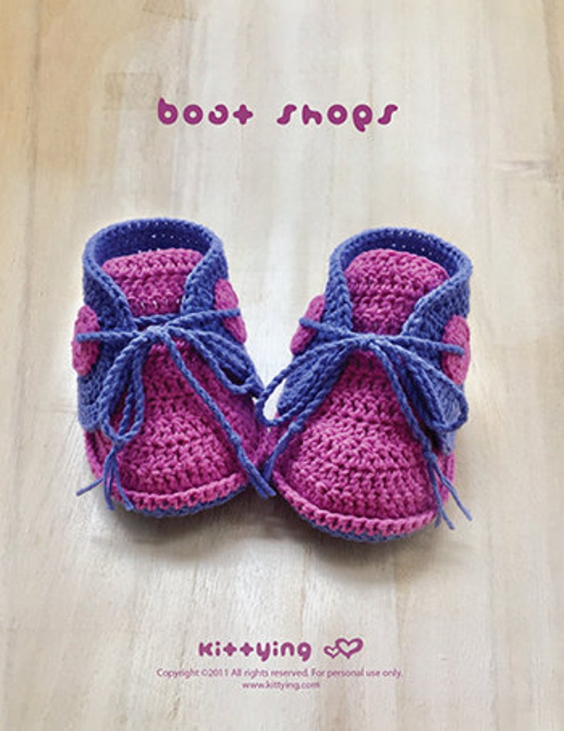 May include: A pair of crocheted baby booties in pink and purple with a blue lace. The booties have a heart-shaped design on the side. The text "bost shops" and "Ki++ying" is visible in the image.