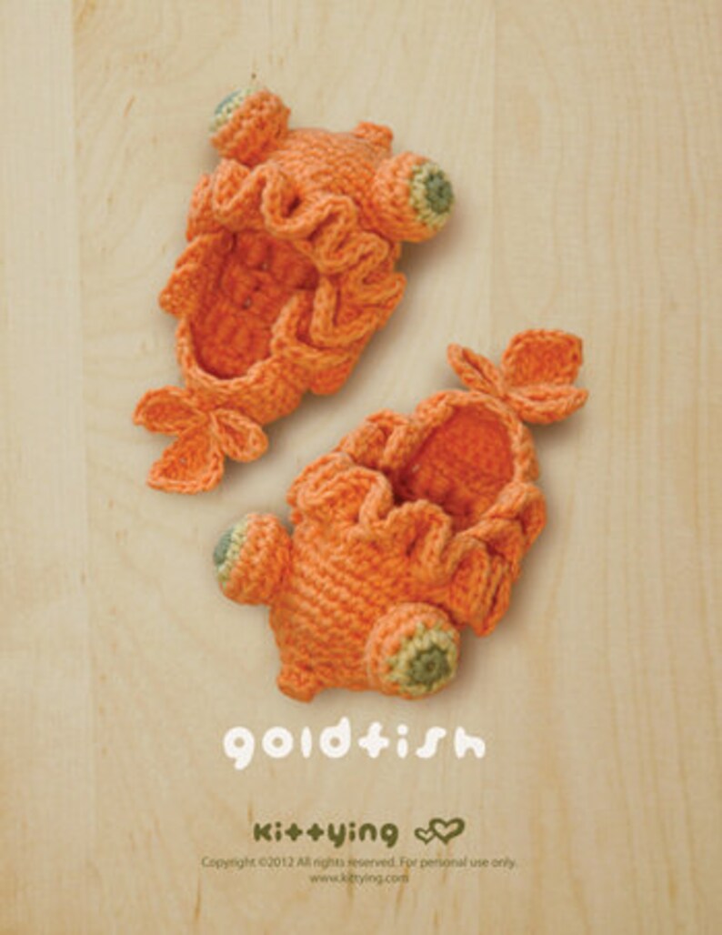 May include: Two handmade, orange crochet goldfish slippers. The slippers have ruffled edges, fins, and green and yellow accents. The word "goldfish" is written in white script below the slippers.