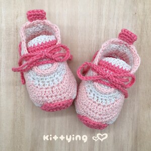 May include: A pair of pink and white crocheted baby booties with a pink ribbon tied around the ankle. The booties have a white crocheted design on the front.