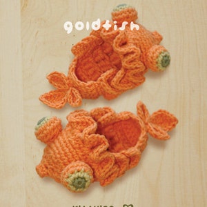 May include: Two handmade orange crochet goldfish, with green and orange accents, are displayed on a light wooden surface. The word "goldfish" is written in white script above the fish. The bottom right corner has the text "kittying" and copyright information.