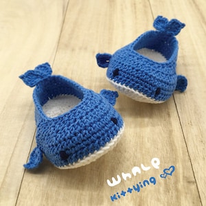 Puede incluir: Un par de zapatos de beb&eacute; de ballena de crochet azul con detalles blancos. Los zapatos tienen un dise&ntilde;o simple con una cola de ballena y una boca blanca. Los zapatos est&aacute;n sobre una superficie de madera con el texto "WHALE Kit+Ying &hearts;" escrito debajo.
