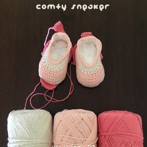 May include: A pair of pink and white crocheted baby booties with a pink yarn ball, a light pink yarn ball, and a darker pink yarn ball. The booties are labeled "comty sn&rho;&omicron;&kappa;&rho;&omicron;" and "Kit+ying".