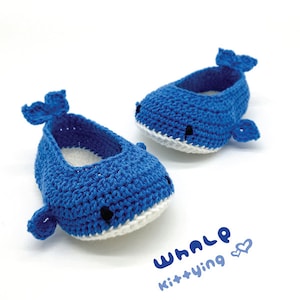May include: A pair of blue crocheted whale baby shoes with white accents. The shoes have a simple design and are perfect for a baby's first steps.