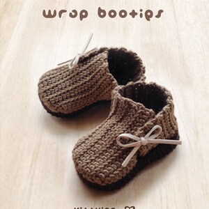 May include: A pair of brown crocheted baby booties with white ribbon ties. The booties are on a light brown wooden surface. The text "wrap bootips" is at the top of the image. The text "Kit+ying" is at the bottom of the image.