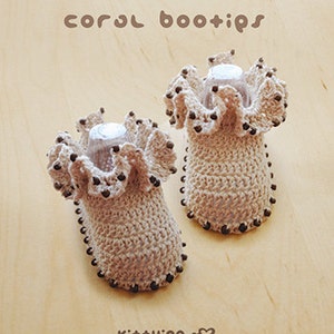 May include: A pair of crocheted baby booties with brown bead accents. The booties are beige and have a ruffled edge. The text "coral bootips" is written above the booties.
