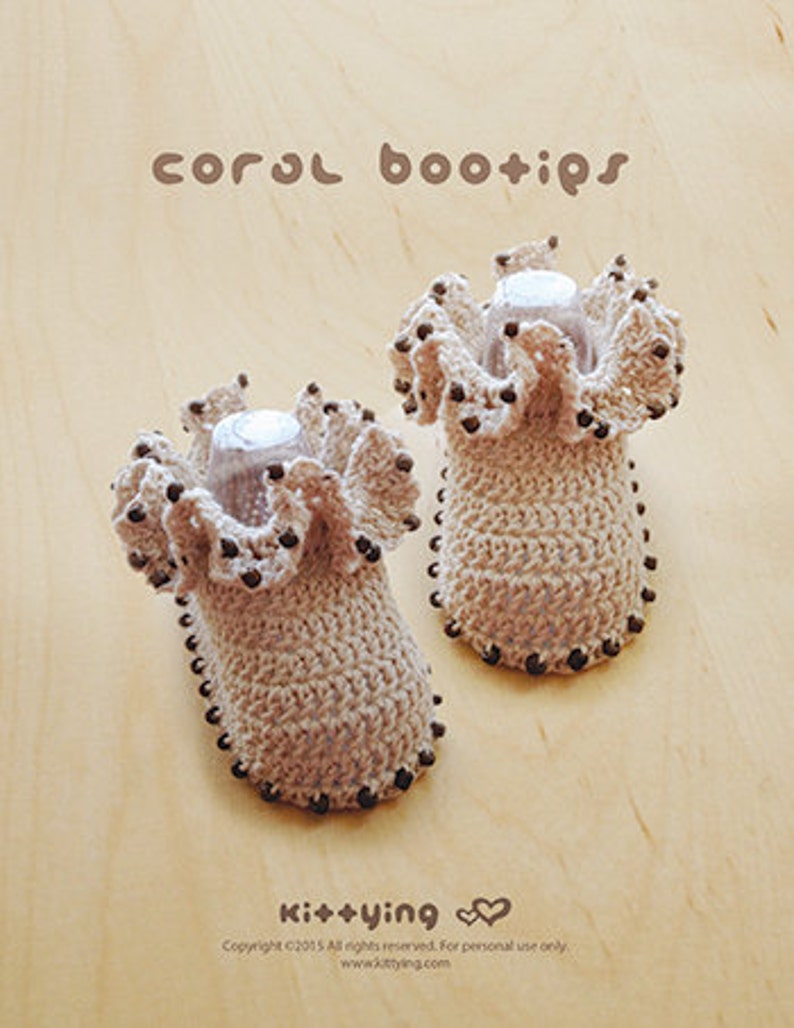 May include: A pair of crocheted baby booties with brown bead accents. The booties are beige and have a ruffled edge. The text "coral bootips" is written above the booties.