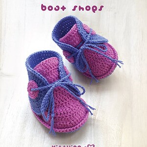 May include: A pair of purple and pink crocheted baby booties with a button detail. The booties are handmade and have a simple design.