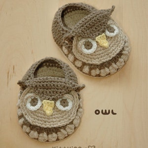 May include: A pair of brown crocheted baby booties shaped like owls. The booties have yellow beaks, white eyes, and brown and beige details.
