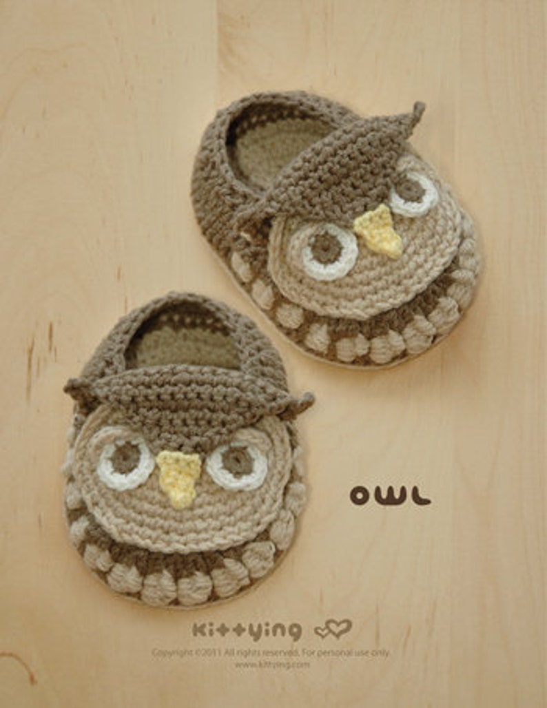 May include: A pair of brown crocheted baby booties shaped like owls. The booties have yellow beaks, white eyes, and brown and beige details.