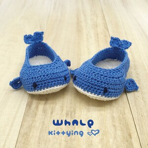 Puede incluir: Un par de zapatos de beb&eacute; de crochet azul con forma de ballenas. Los zapatos tienen detalles blancos y ojos negros. El texto "WHALE Kittying" est&aacute; impreso debajo de los zapatos.