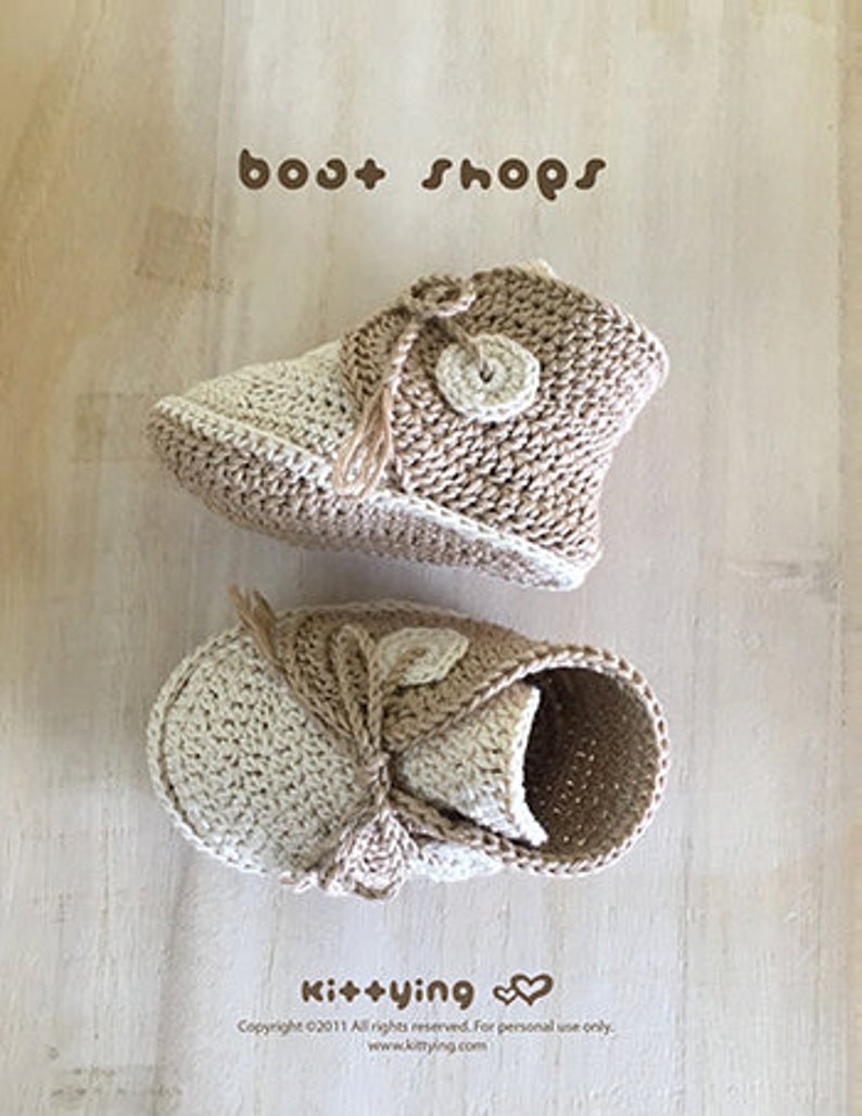 May include: A pair of crocheted baby booties in beige and cream with a button detail. The booties are tied with a beige ribbon and have the text "bost shops" and "Kit+ying" on the image.
