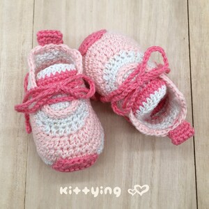 May include: A pair of pink and white crocheted baby shoes with laces. The shoes have a striped pattern and are tied with a pink ribbon.