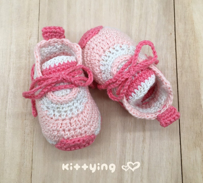 May include: A pair of pink and white crocheted baby shoes with laces. The shoes have a striped pattern and are tied with a pink ribbon.