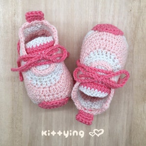 May include: A pair of pink and white crocheted baby shoes with pink laces. The shoes have a striped pattern and are tied with a bow.