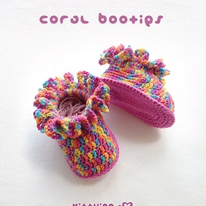 May include: A pair of colorful crocheted baby booties with a pink base and a ruffled edge. The booties are made with a variety of colors, including pink, yellow, blue, and orange. The text "coral bootips" is written in pink letters at the top of the image. The text "Kit+ying" is written in pink letters at the bottom of the image.