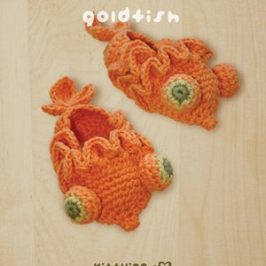 May include: Two handmade orange crochet goldfish, with green and tan accents, are displayed on a light wood surface. The word "goldfish" is above the fish. The bottom of the image has the text "kittying" and copyright information.