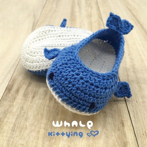 Puede incluir: Un par de botines de beb&eacute; de crochet azul y blanco con forma de ballenas. Los botines tienen una barriga blanca y una espalda azul con un contorno blanco. El texto "whale kittying" est&aacute; escrito debajo de los botines.