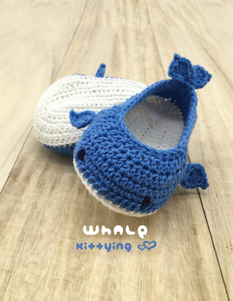 Puede incluir: Un par de botines de beb&eacute; de crochet azul y blanco con forma de ballenas. Los botines tienen una barriga blanca y una espalda azul con un contorno blanco. El texto "whale kittying" est&aacute; escrito debajo de los botines.