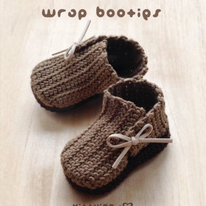 May include: A pair of brown crocheted baby booties with white ribbon ties. The booties are made with a textured stitch and have a simple, classic design.
