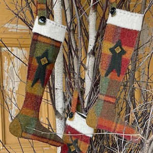 Pode incluir: Três meias de Natal feitas à mão de feltro com um padrão xadrez em tons de vermelho, verde, marrom e dourado. Cada meia apresenta uma estrela de feltro preto com uma fita de feltro preto.