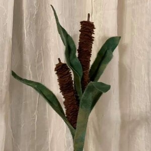 Peut inclure: Une bouteille en grès brun avec un arrangement de fleurs en feutre vert et brun. La bouteille a un fond arrondi et un col étroit.