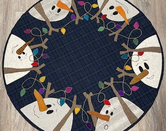May include: A blue and white quilted Christmas tree skirt with five snowmen around the edge. Each snowman has a carrot nose, black eyes, and a red button. The snowmen are holding strings of colorful lights.
