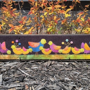 May include: A felt wall hanging with a row of colorful birds with button eyes and flowers. The birds are in shades of yellow, orange, blue, purple, and green.
