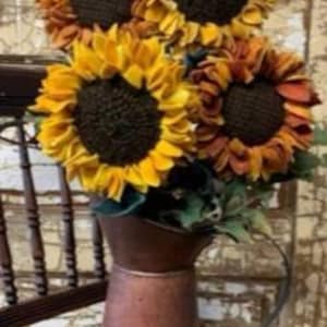 May include: A bouquet of four faux sunflowers in shades of yellow and orange arranged in a copper pitcher.