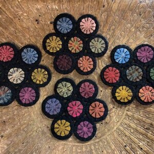 May include: Set of six colorful wool felt flower coasters with black edging. Each coaster features a circular design with a central circle surrounded by smaller circles.