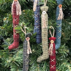May include: Six handmade felt Christmas ornaments in the shape of stockings. The stockings are in various colors and patterns, including red, blue, green, and brown. Each stocking has a button and a tassel at the top.