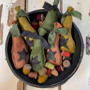 May include: A black bowl filled with felt pears and acorns. The pears are in shades of green, brown, and yellow with black star accents. The acorns are in shades of brown, red, and green.