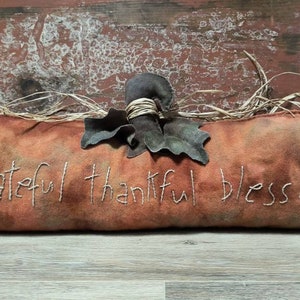 May include: A brown felt pumpkin with the words "grateful thankful blessed" embroidered on it. The pumpkin has a green felt leaf and a brown twine stem.