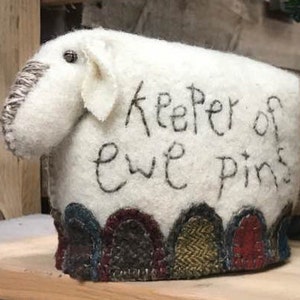 May include: White felt sheep pincushion with the text "Keeper of ewe pins" embroidered on the front. The sheep has a brown felt nose and a brown felt ear. The bottom of the sheep is decorated with colourful felt patches.