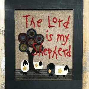 Puede incluir: Un tapiz de pared de punto de aguja enmarcado con el texto "The Lord is my Shepherd" en bordado rojo. El diseño presenta un árbol con círculos coloridos y tres ovejas con estrellas amarillas.