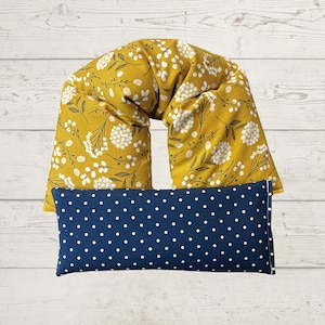 May include: Mustard yellow neck wrap with a white floral pattern and a navy blue rectangular pillow with white polka dots. The neck wrap is designed to conform to the neck and shoulders. The pillow is rectangular.