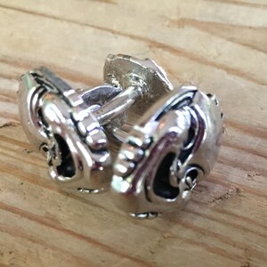 May include: A pair of silver cufflinks with a detailed design of a face on each cufflink.
